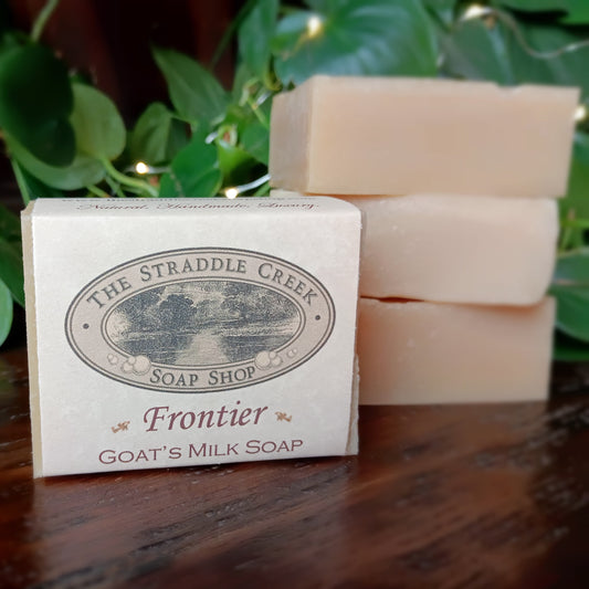 Stack of goat's milk soap bars with a bar labeled 'The Straddie Creek Soap Shop' on a wooden surface with greenery in the background.